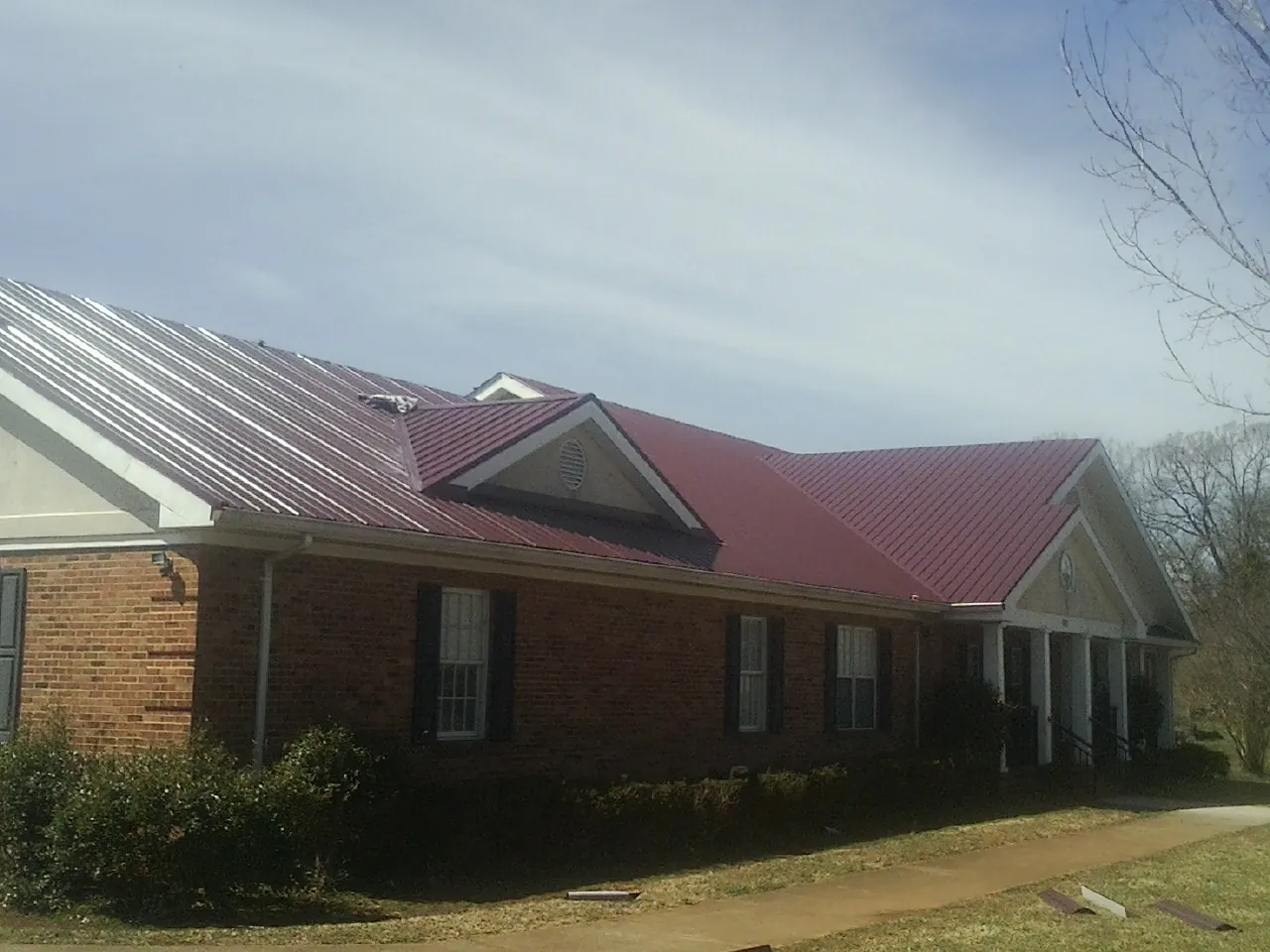 Red metal roof with gabled entries on a long brick building, from a Hail Damage Roof Repair job in Porter
